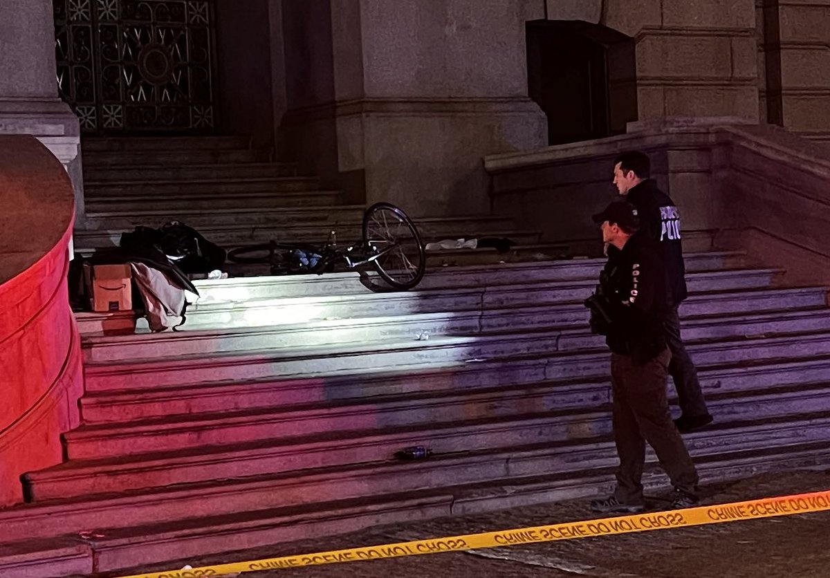 Crime scene tape surrounds the staircase at the front of Providence City Hall. Detectives are currently on scene investigating a reported stabbing. A bicycle and other belongings are scattered across the stairs, facing Kennedy Plaza